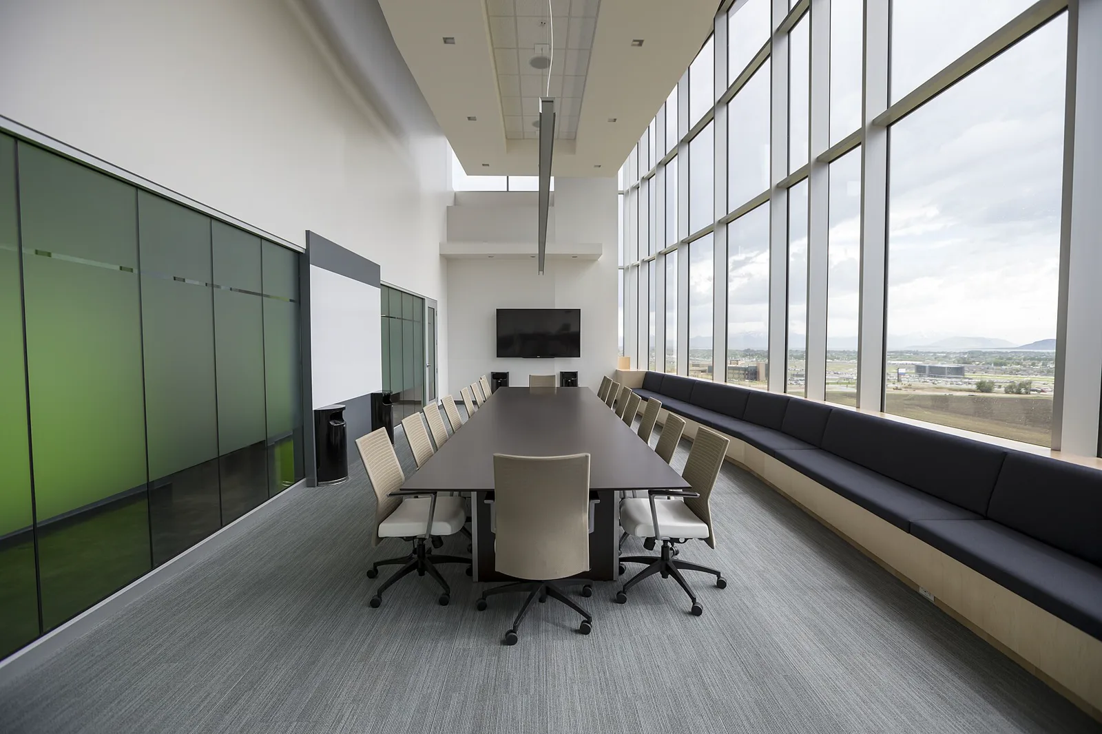 An empty boardroom with a long table beside floor-to-ceiling windows